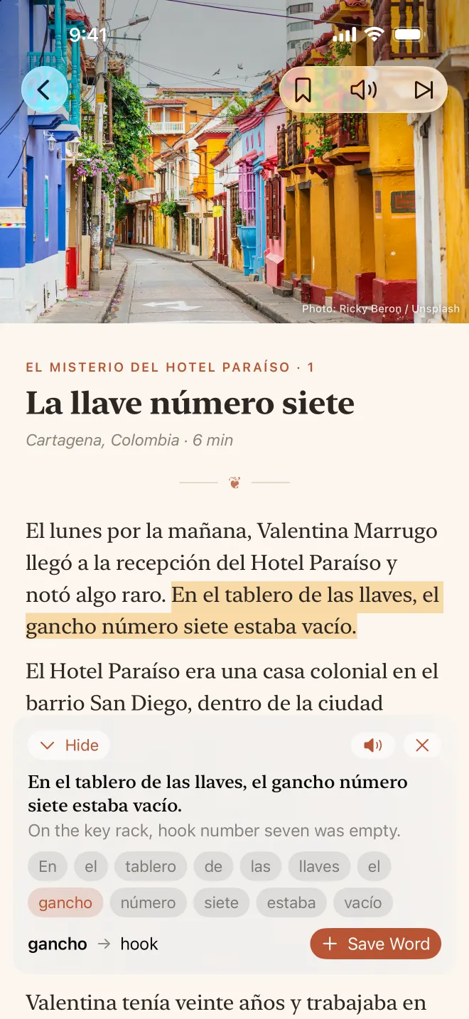 Facing Pages on a portrait iPhone, open at El misterio del Hotel Paraíso with a photo of Cartagena. The sentence “En el tablero de las llaves, el gancho número siete estaba vacío.” is shown with its English translation, and the word “gancho” is looked up as “hook”.